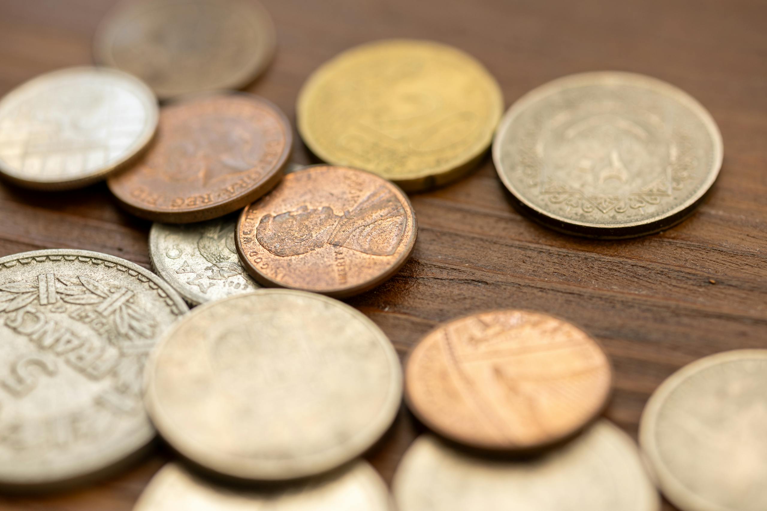A detailed close-up image showing various vintage coins scattered on a wooden surface, capturing their unique textures and engravings.